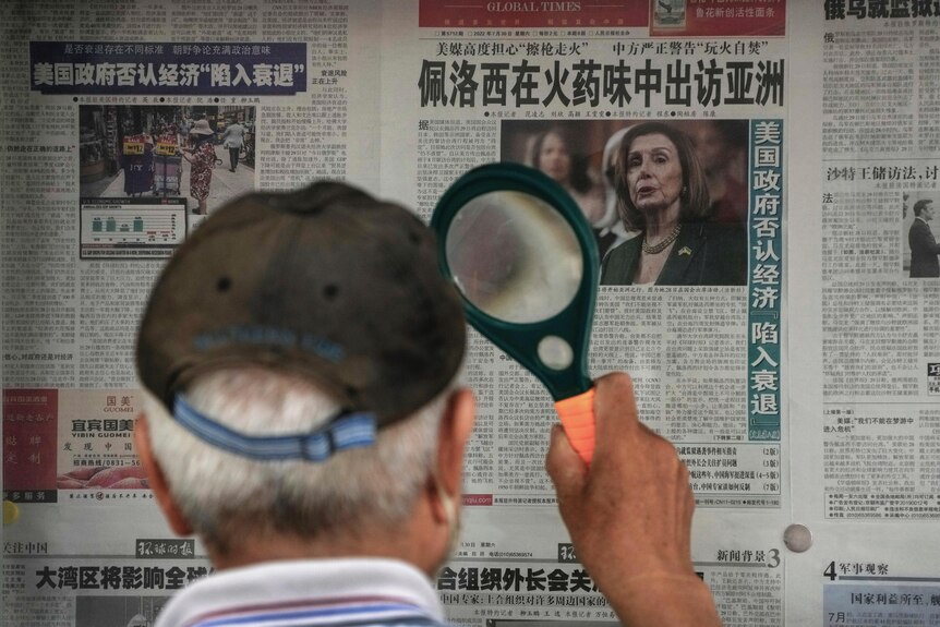 Man uses magnifying glass to read newspaper article with image of Nancy Pelosi.