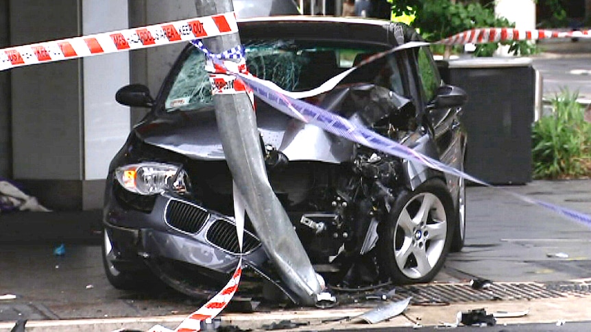 Wreckage of a BMW car sits against a bent street pole.