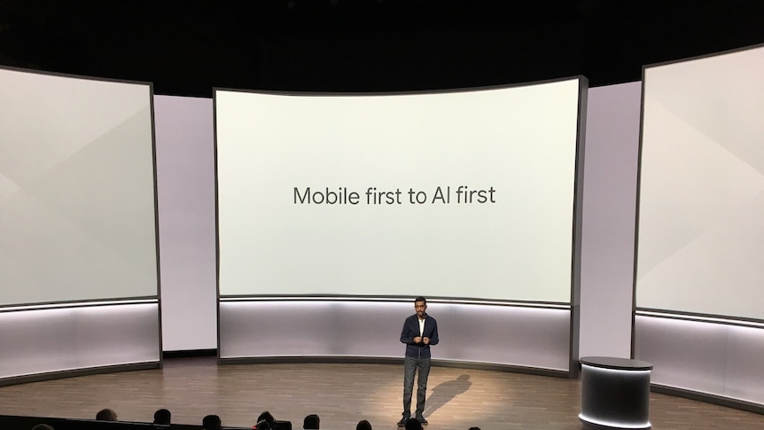 Google CEO Sundar Pichai on stage with "Mobile first to AI first" on big screen.