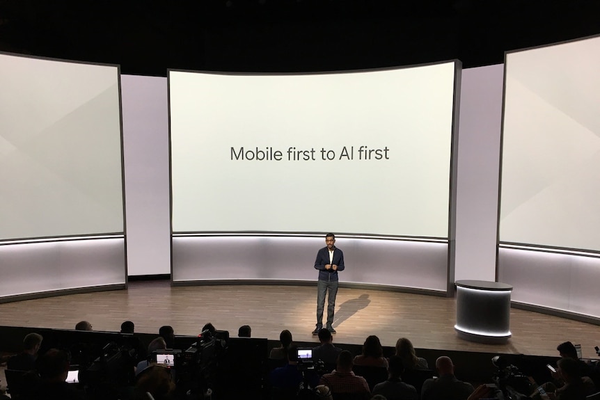 Google CEO Sundar Pichai on stage with "Mobile first to AI first" on big screen.