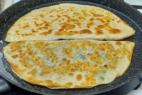 Two semicircles of fried bread cook in a pan of oil