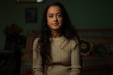 Woman wearing brown sweater sitting down in living room.