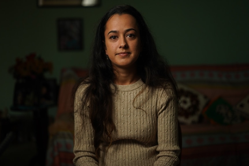 Woman wearing brown sweater sitting down in living room.