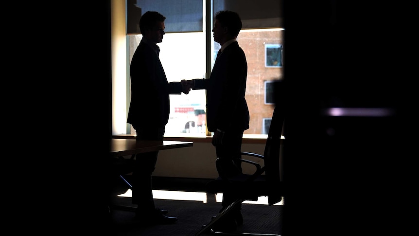 Two men can be seen through an open door shaking hands.