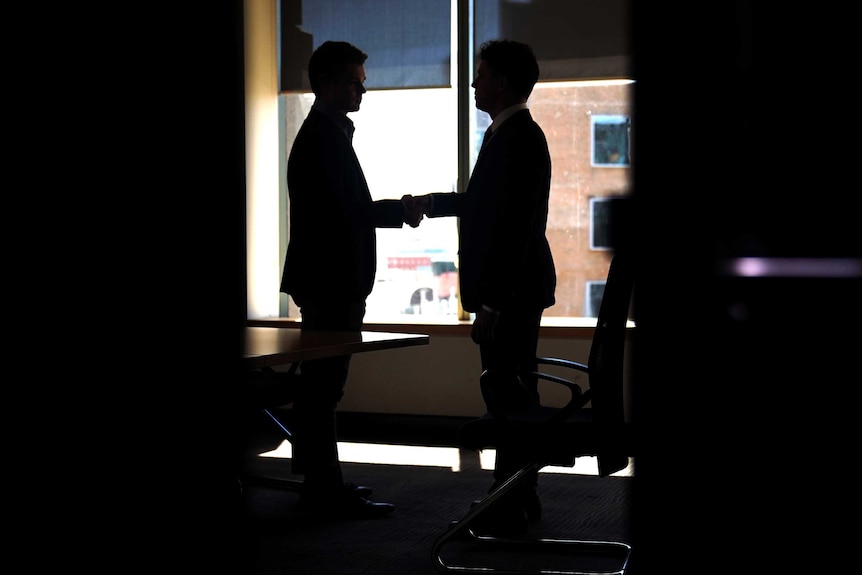 Two men can be seen through an open door shaking hands.