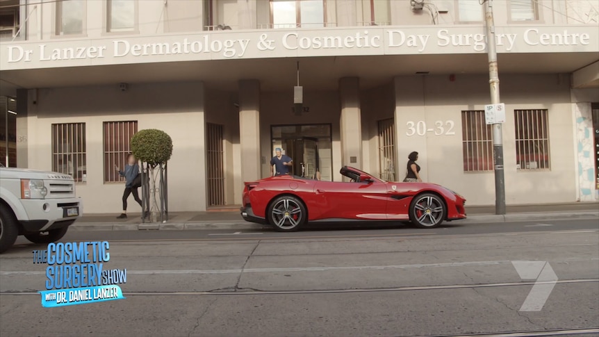 A red sports car parked in front of a building with the sign 'Dr Laner Dermatology & Cosmetic Day Surgery Centre'.