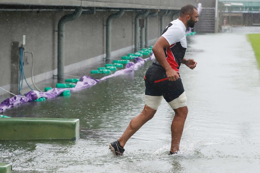A rugby player in training gear runs through an area flooded to his ankles.