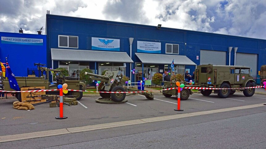 The exterior of the Hearts4Heros cafe and op shop in a large, blue warehouse type building with military vehicles in front.