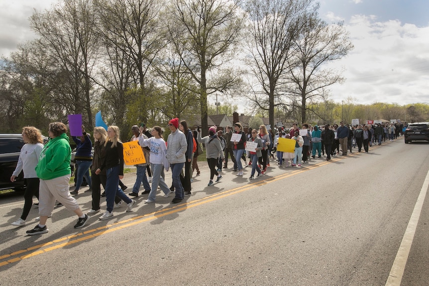 Hundreds of people march down one side of the road in protest of a teen being shot.
