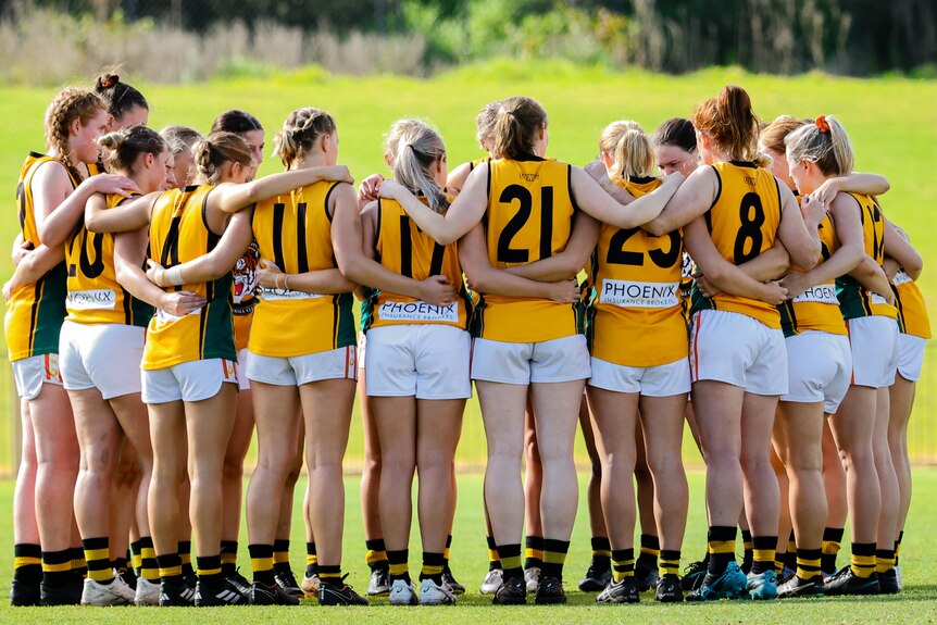 Curtin Uni Wesley players stand arm in arm in a huddle during an Aussie rules match.