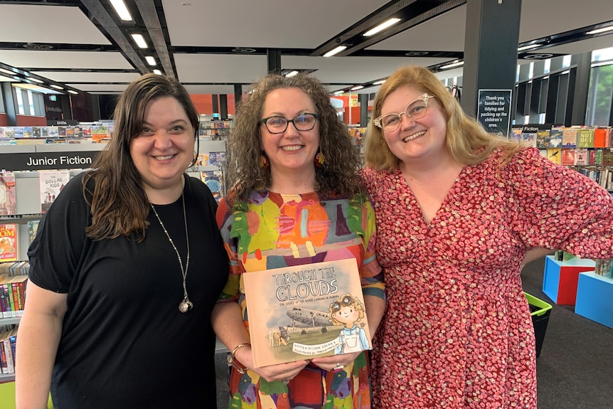 Editor Michelle Fracaro, author Carm Hogan and illustrator Pinky Whittingslow stand in a library space.