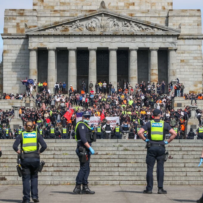 From behind a police line, you view the steps of Melbourne's Shrine of Remembrance swarming with protesters on an overcast day.