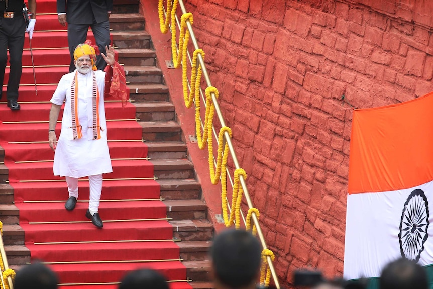Mr Modi, wearing white and orange, walks down a red carpet staircase at the Red Fort in Delhi.