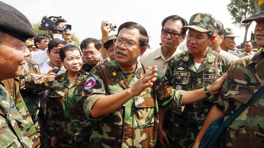 Hun Sen stands dressed in army fatigues speaking to a group of people