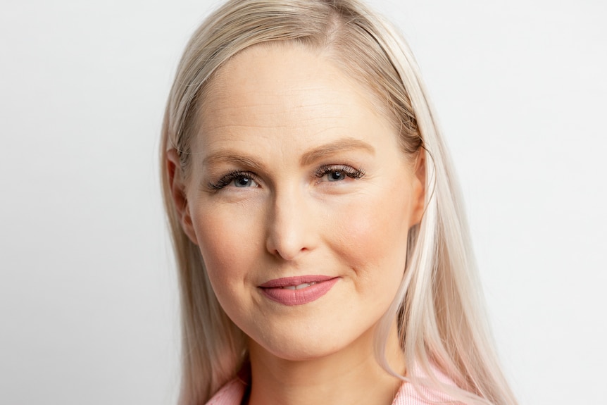 A closeup of a woman with blonde hair wearing a light pink collared shirt.