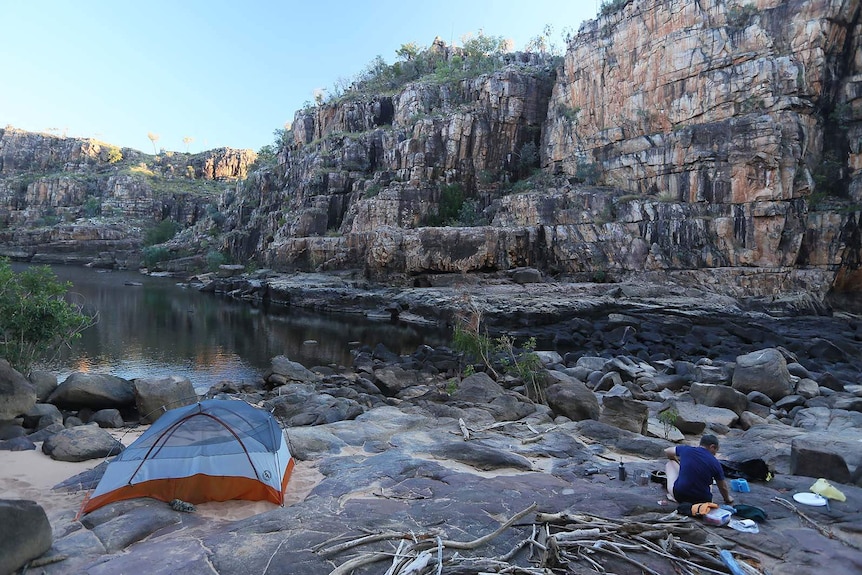 A man and his tent on the backs of a river in remote and rocky terrain
