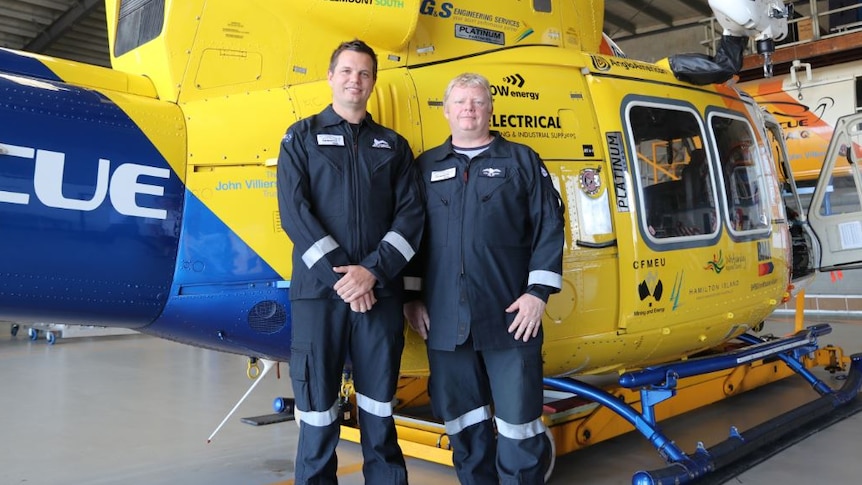 Ben McCauley and Kevin Berry stand in front of the RACQ rescue helicopter in its hanger.