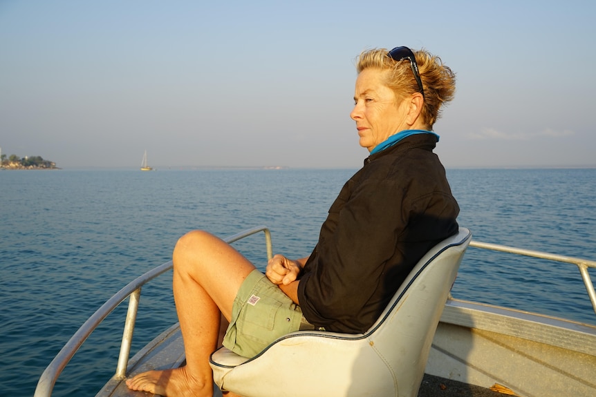 a woman with short blonde hair on a boat looking at the ocean
