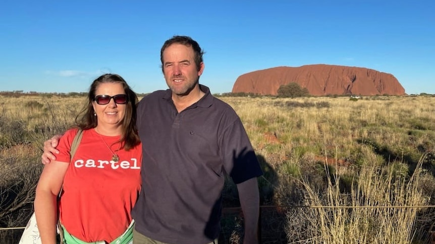 A woman & a man near Uluru in Northern Territory. She has long, dark hair & is wearing a red top. He is in a brown jumper.
