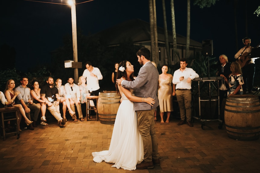 A man and a woman in a white wedding dress dance at together.