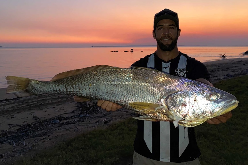 Footballer Alex Aurrichio shows a large fish he caught at sunset on a flotsam-strewn beach