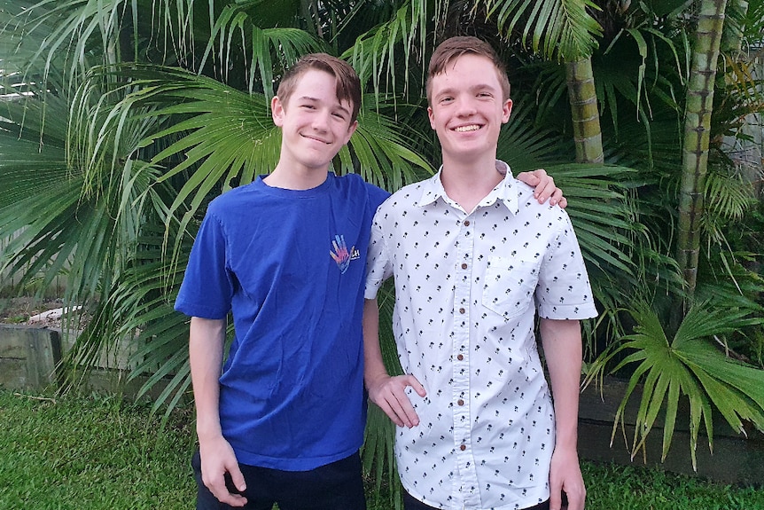 Two teenage boys, one in t shirt the other in button up shirt. Both are smiling. they are standing close