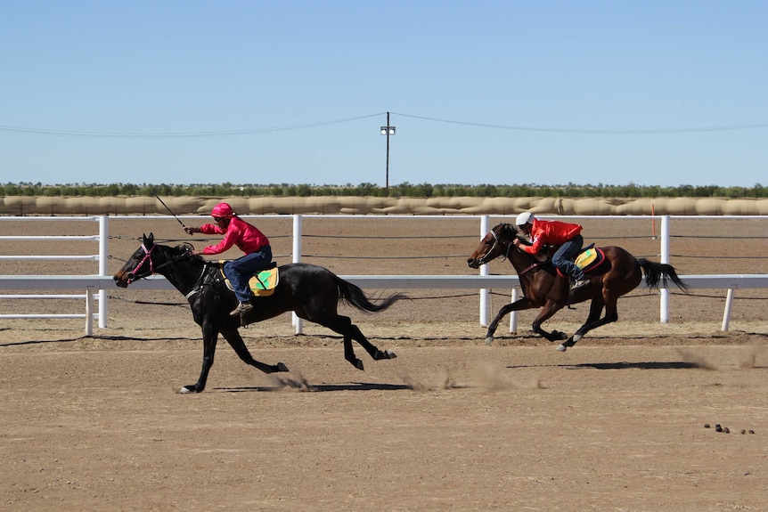 Two people on horses racing on a dirt track.