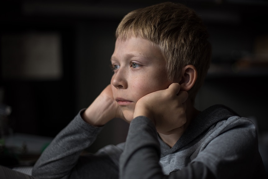 Close-up photo from 2018 film Loveless of Matvey Novikov with hands on chin, arms resting on table and looking into the distance