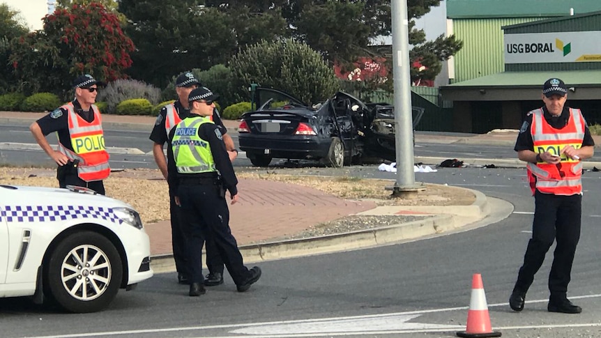 Police standing on the street with a crashed black Ford