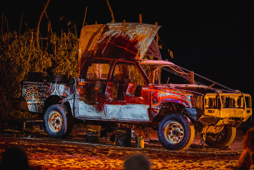 An old car wreck decorated with paintings and lit up with colourful lights.