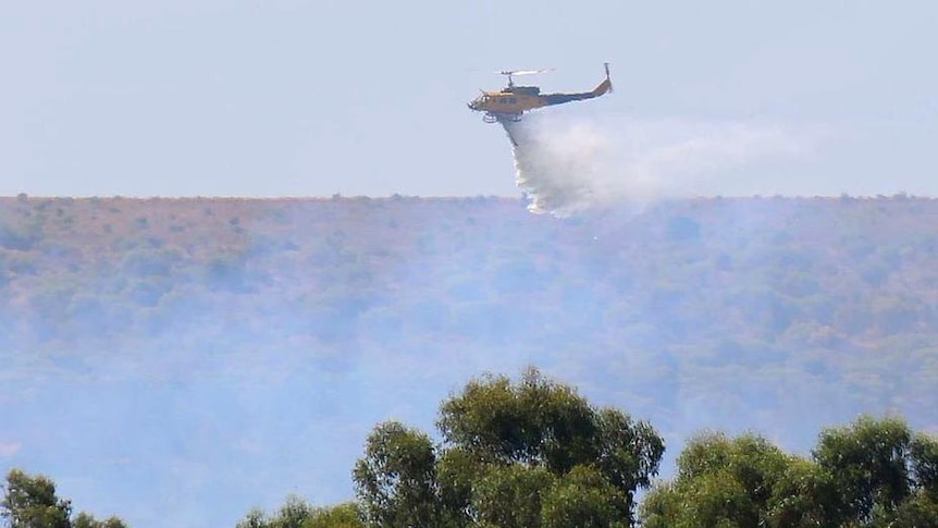 A helicopter water bomber dumps its load on a bushfire