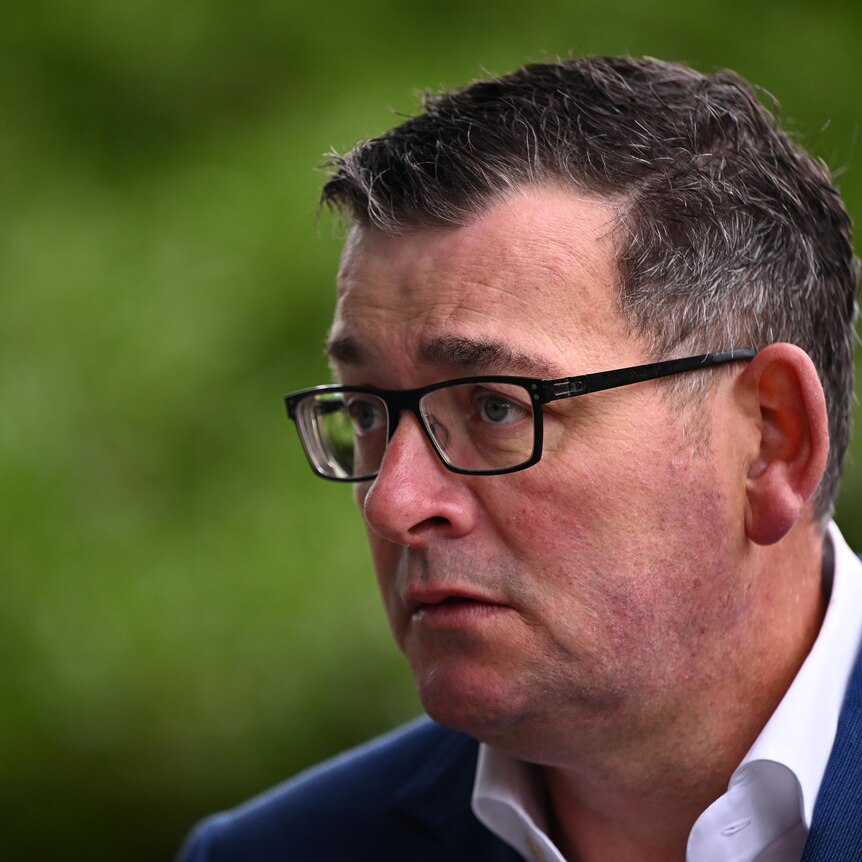 Daniel Andrews appears serious, dressed in a white shirt and blue jacket as he stands outside.