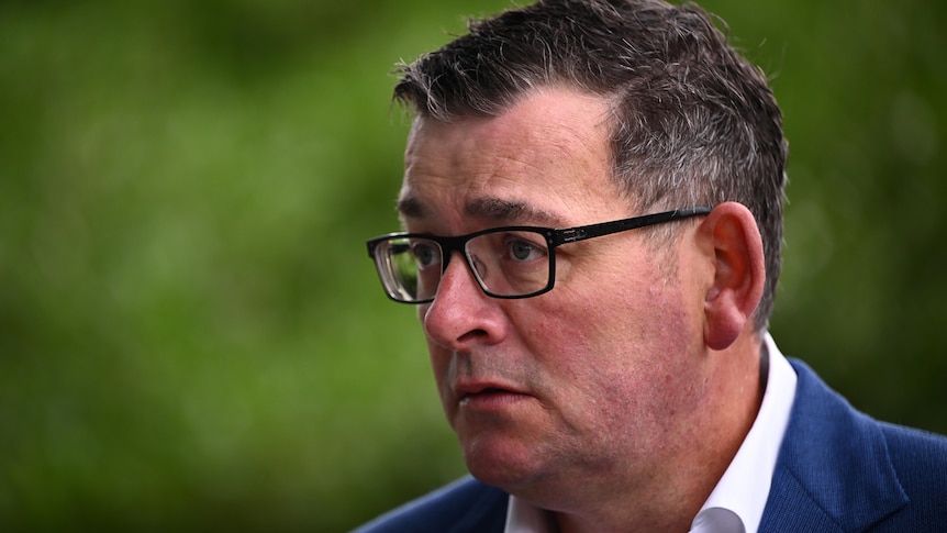 Daniel Andrews appears serious, dressed in a white shirt and blue jacket as he stands outside.