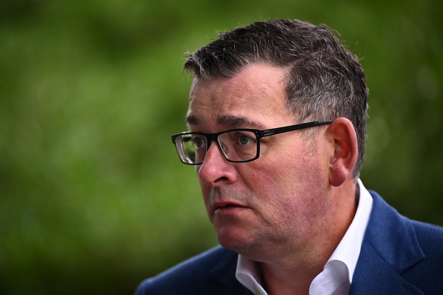 Daniel Andrews appears serious, dressed in a white shirt and blue jacket as he stands outside.