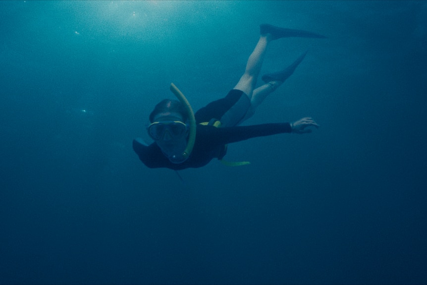 Underwater photo of a young woman diving. She is wearing a snorkel and goggles, wetsuit, and flippers.
