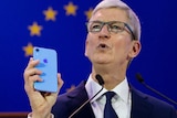 Apple CEO Tim Cook holds up an iPhone.