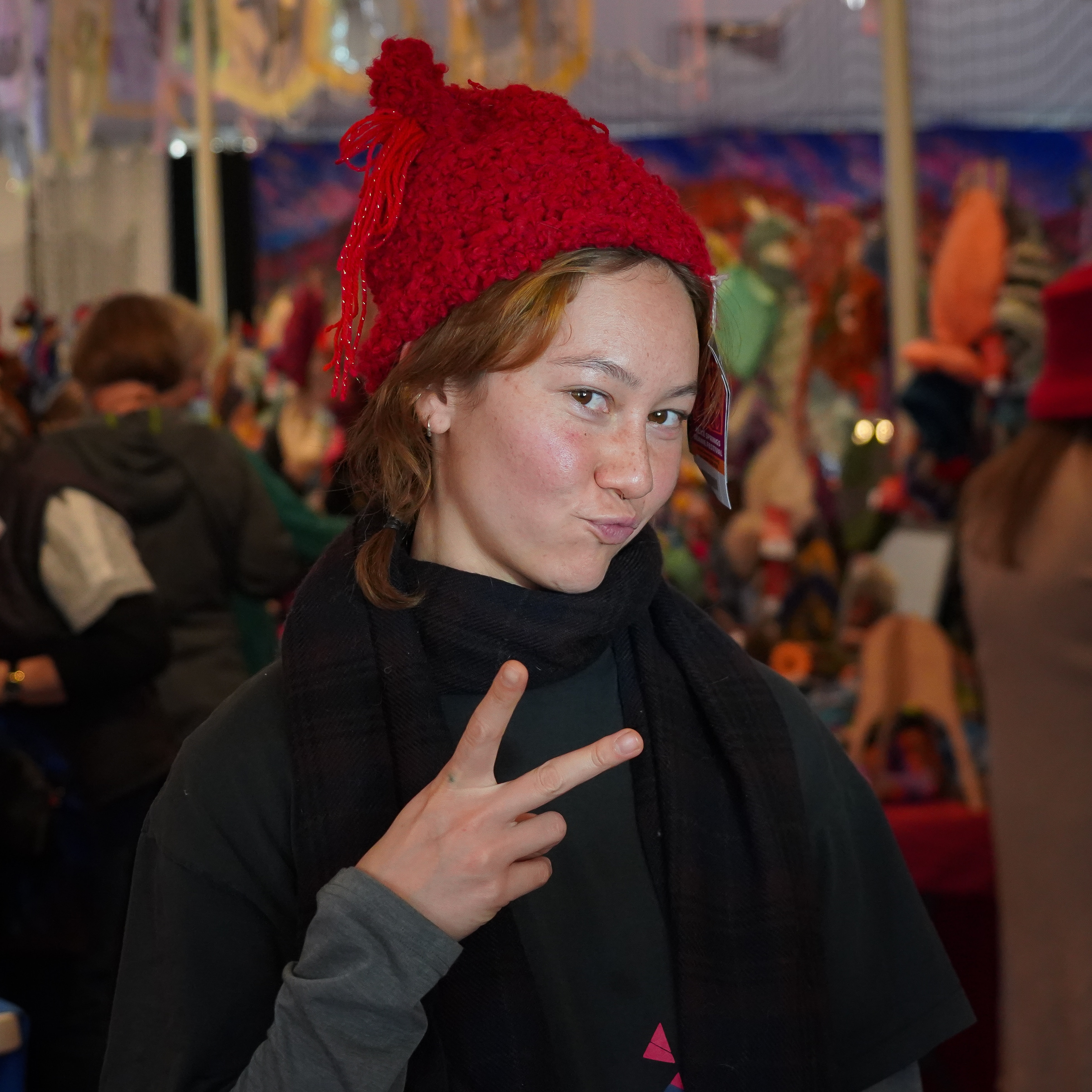 A girl doing a peace sign while posing for the camera wears a red, knitted beanie on her head.