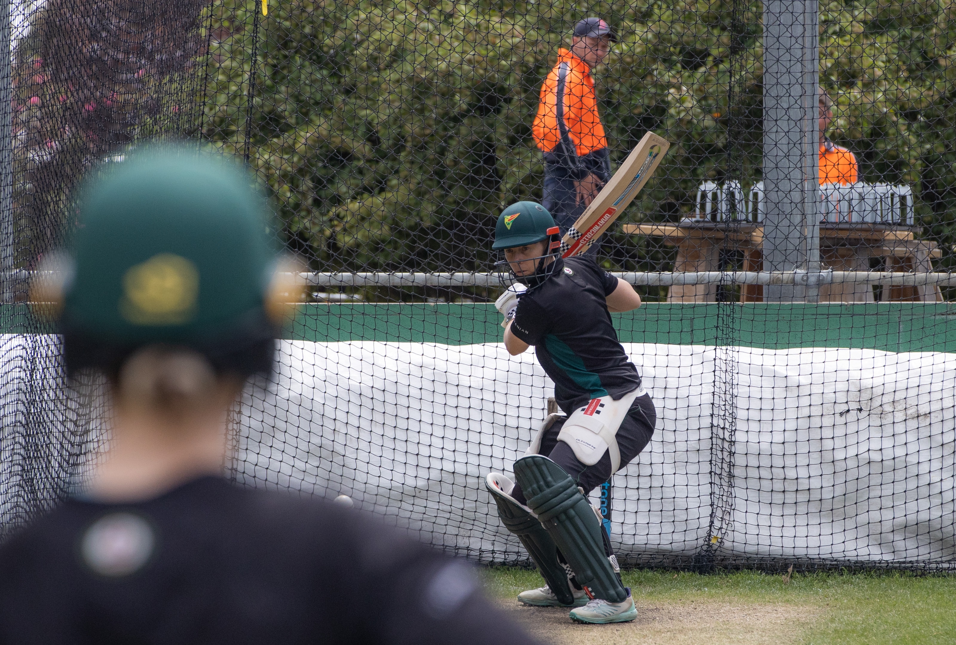 Una mujer se prepara para lanzar una pelota de críquet a la red. 