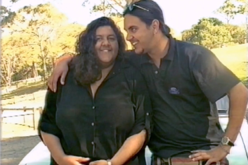 A blurred older photo of a young man and woman ijn black shirts smiling, the man with his arm around the shoulder of the woman.