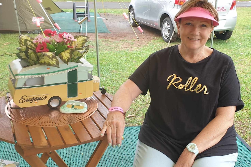 A woman sits at a round outdoor table with a mini vintage van centrepiece wearing a 'Roller' T-shirt and pink visor.
