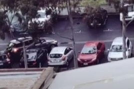 A screenshot of a police man being thrown by a reversing car onto other parked cars.