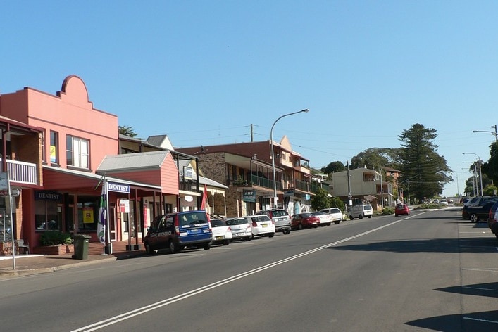 A wide, main street in a coastal town showing a historic-looking, peach-coloured shopfront.