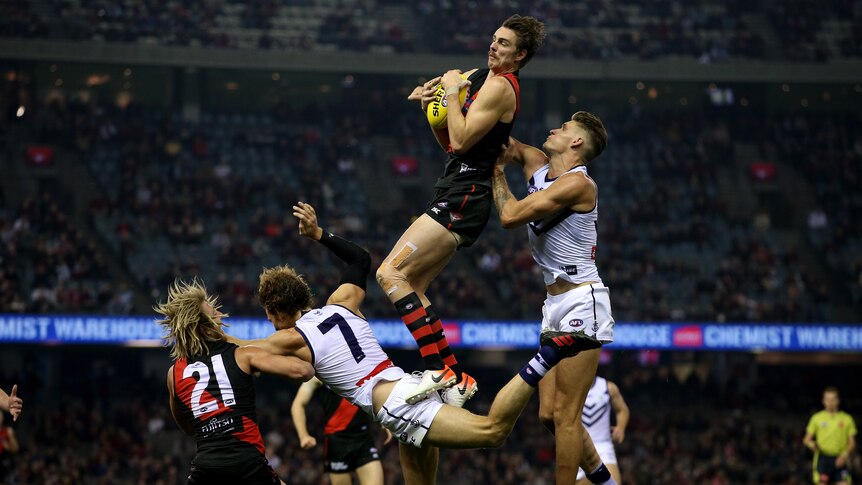 Joe Daniher holds onto a yellow football after leaping into the air with three other players scattered around him