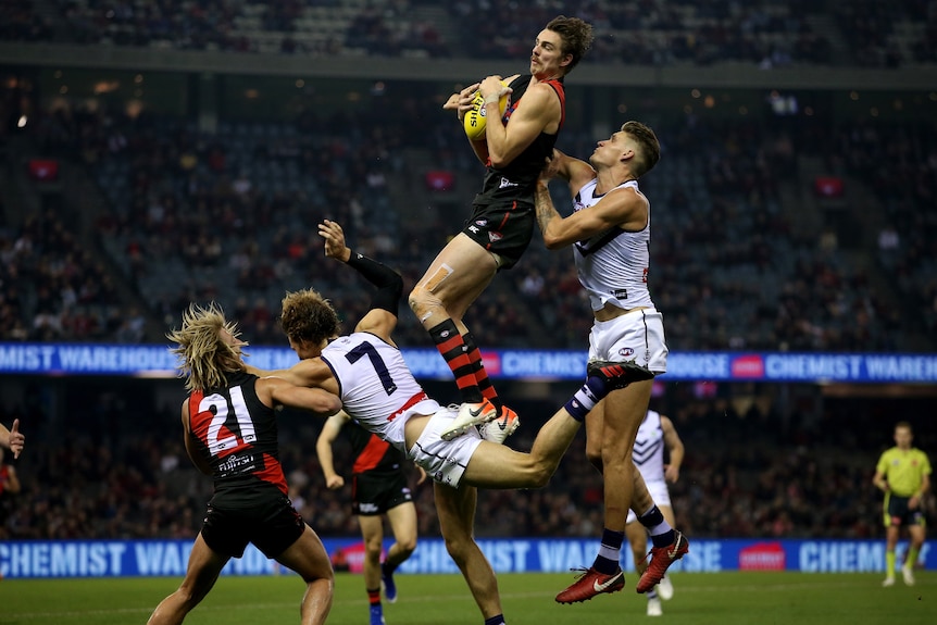 Joe Daniher holds onto a yellow football after leaping into the air with three other players scattered around him