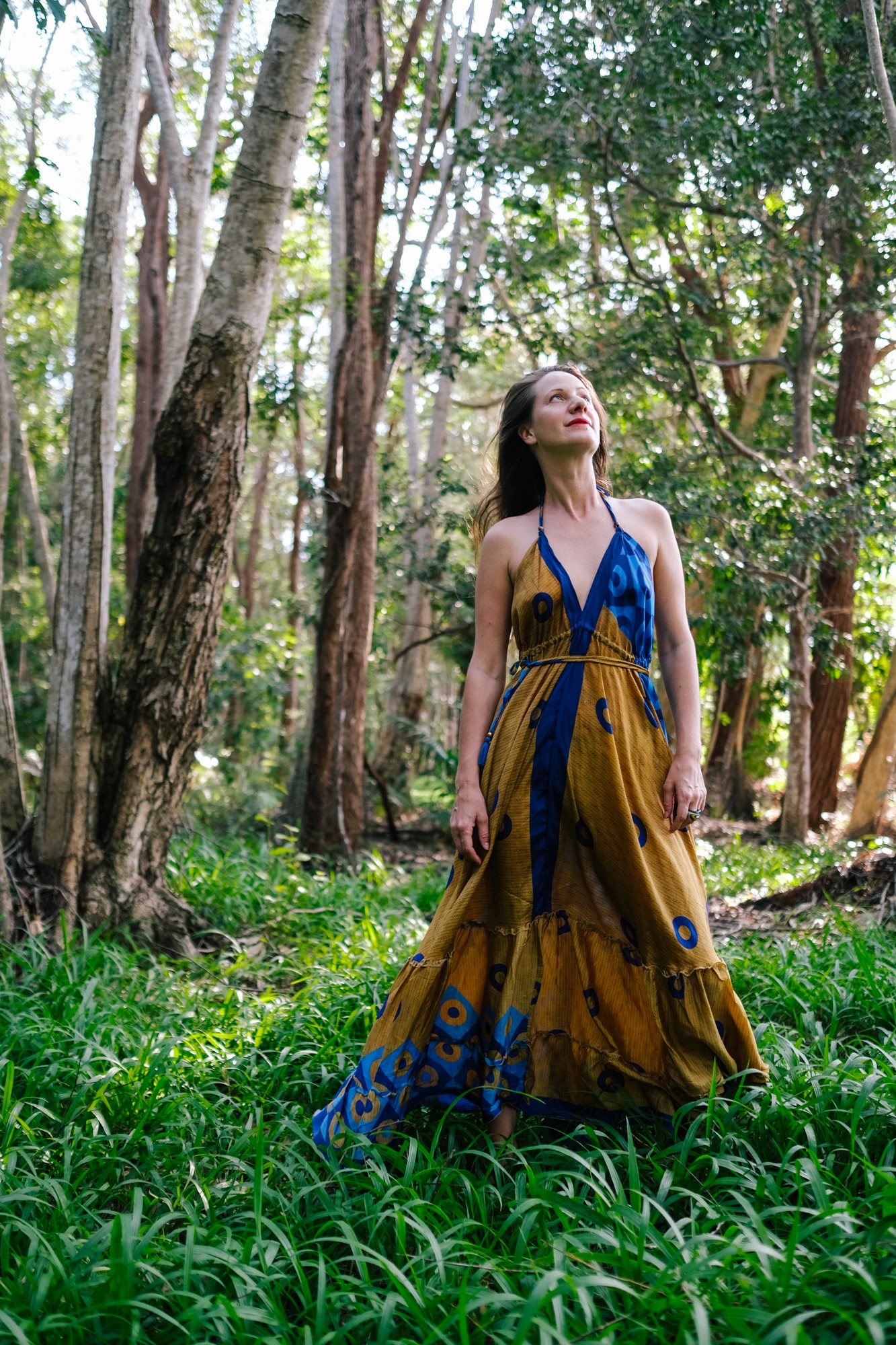 Nara Walker wears a long colourful dress and stands in rainforest near her house, looking up