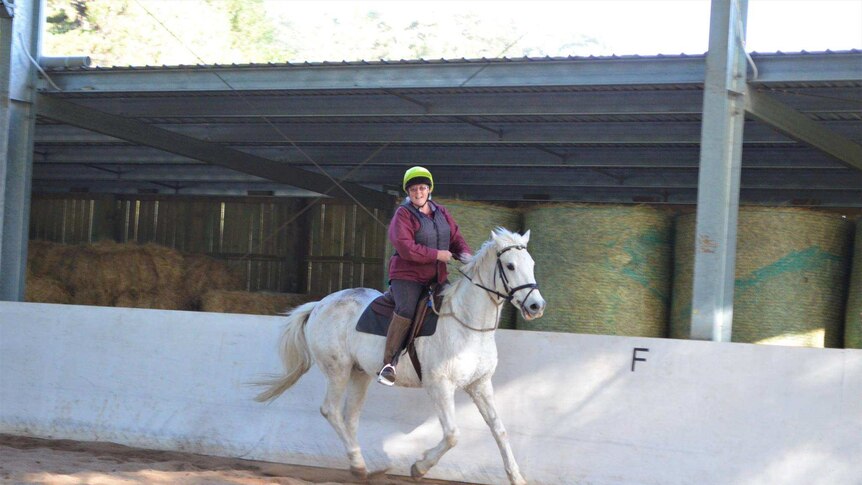 Woman riding a white horse in a horse riding arena