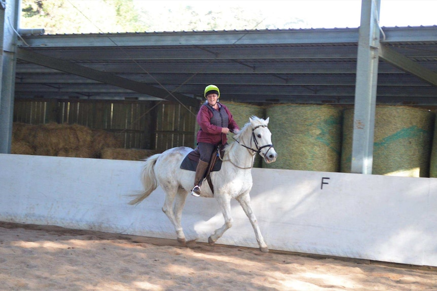 Woman riding a white horse in a horse riding arena