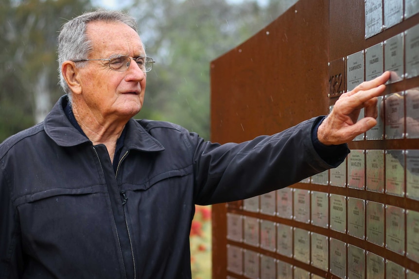 Bruce Pennay touching a special wall with plaques on it at Bonnegilla.