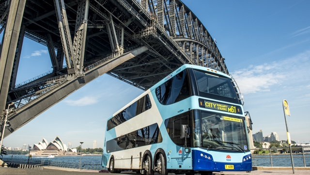A double-decker bus parked under the Sydney Harbour Bridge.