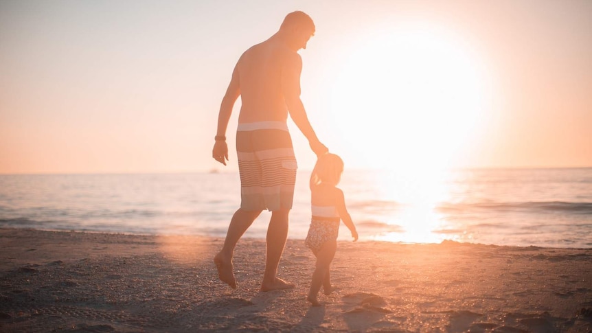 Father walking on the beach with daughter for story on men's experiences with parental leave.